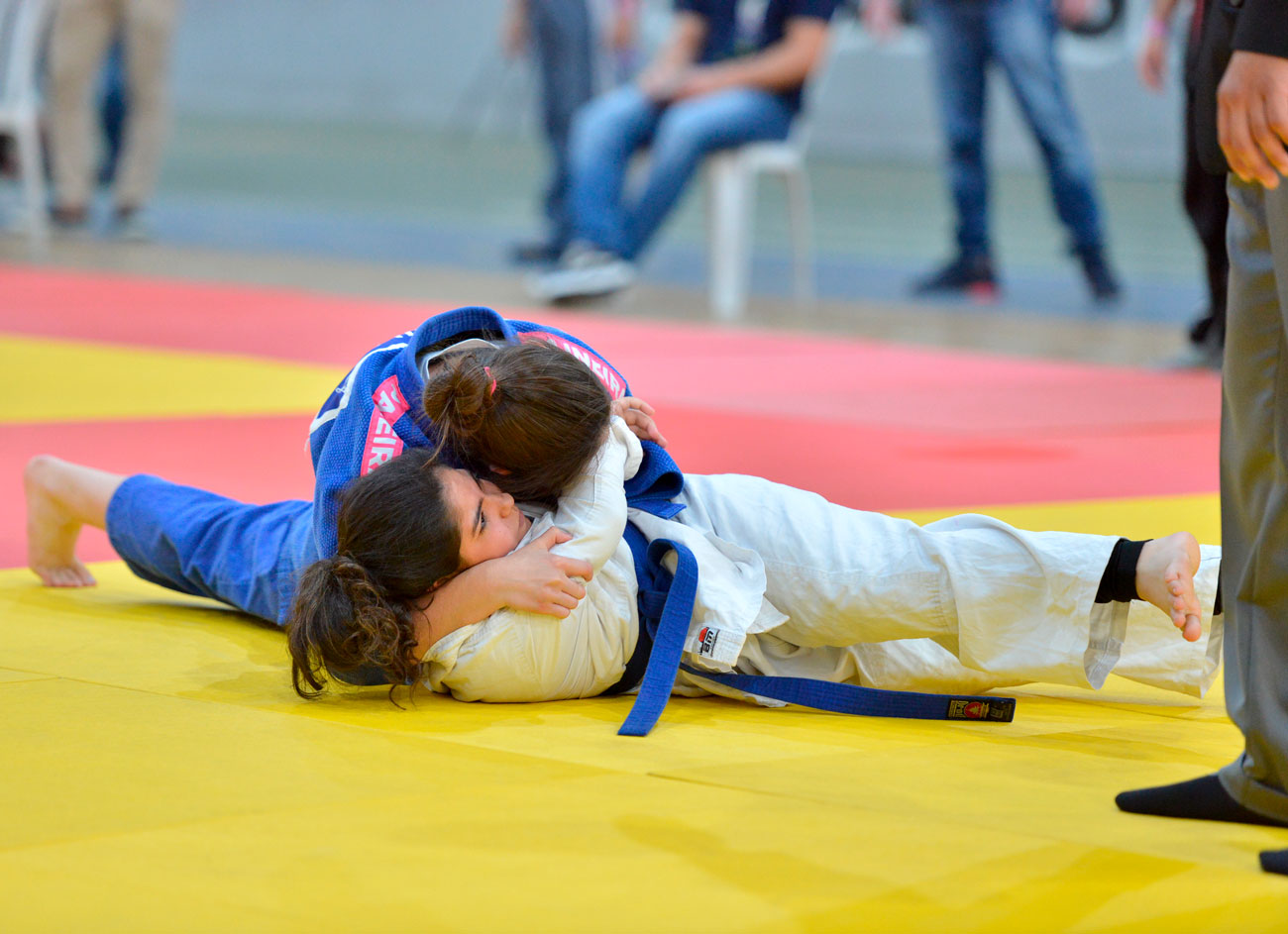 Uma mulher luta com outra em uma competição de jiu-jitsu, mostrando a qualidade e a força do judô da 1ª Delegação Regional da Capital.