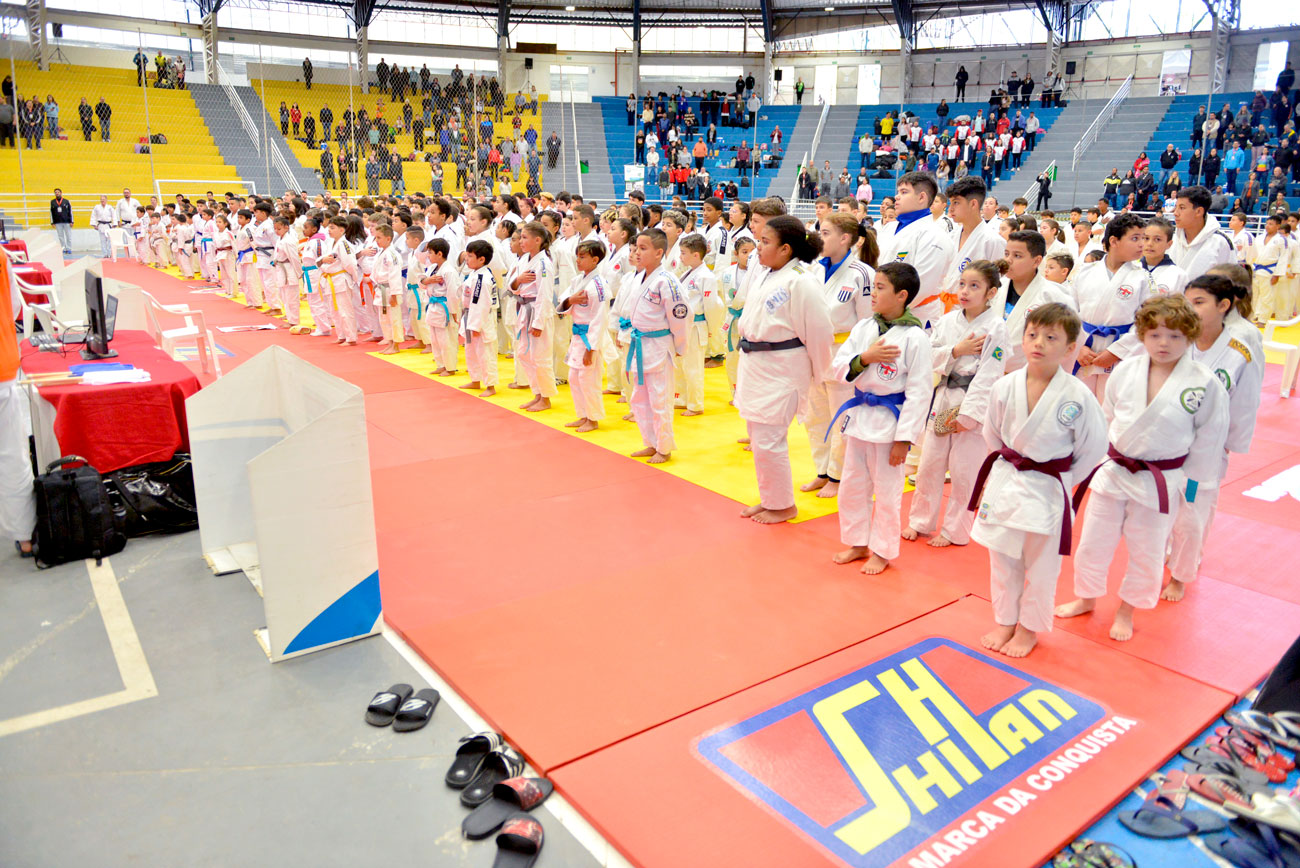 Um grupo de crianças com uniformes tradicionais de karatê em pé em um ginásio para a 72ª edição do Torneio Budokan, marcando história e o segundo ano transformador de uma parceria.