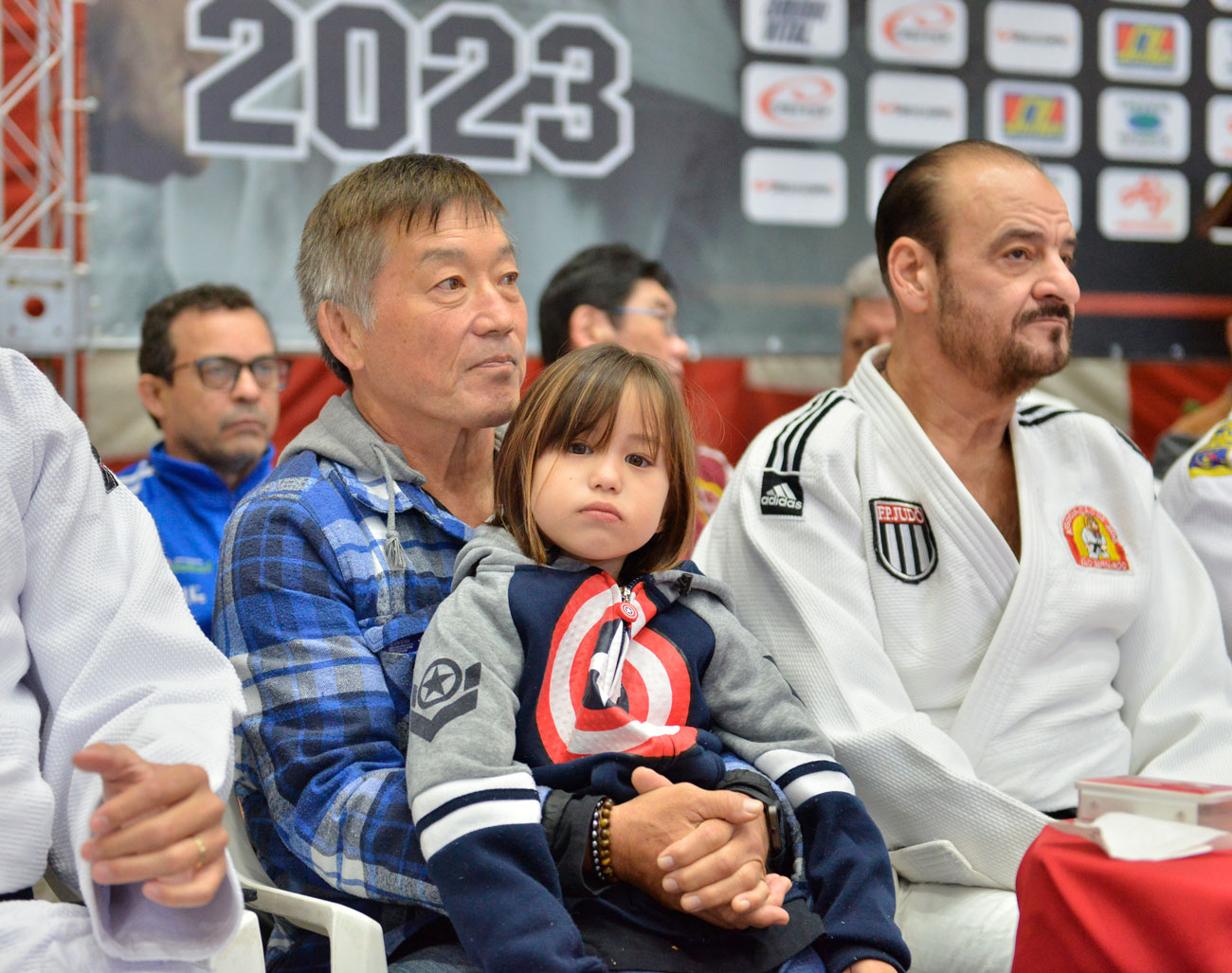 Um grupo de homens e uma criança sentados um ao lado do outro, mostrando tradição e história na 72ª edição do Torneio Budokan.