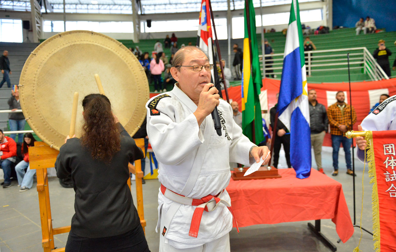 Um homem falando ao microfone durante a 72ª edição do Torneio Budokan, enfatizando o significado histórico da parceria transformadora.