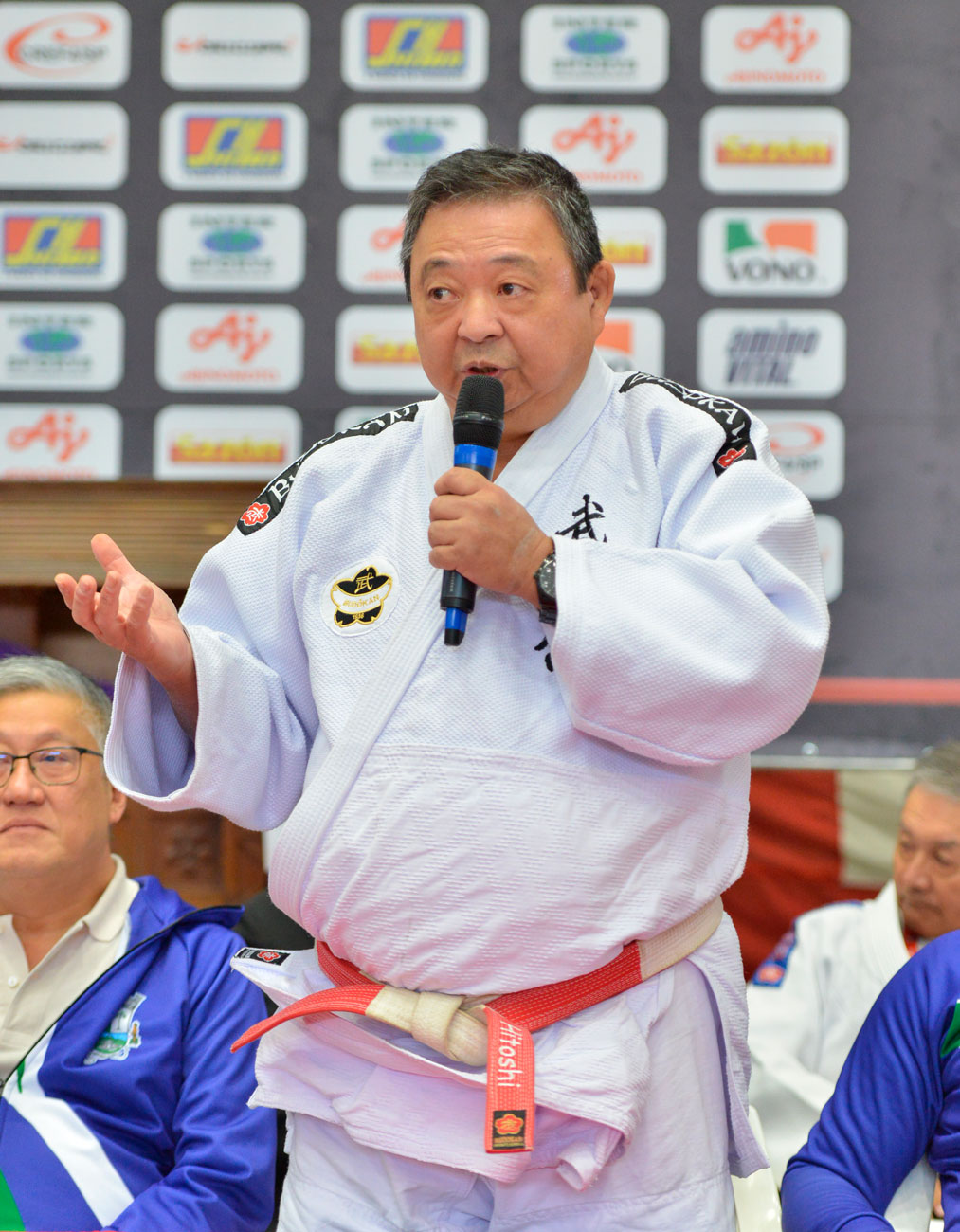 Um homem com uniforme de judô participando da 72ª edição do Torneio Budokan, mostrando tradição e história através de suas palavras ditas ao microfone.